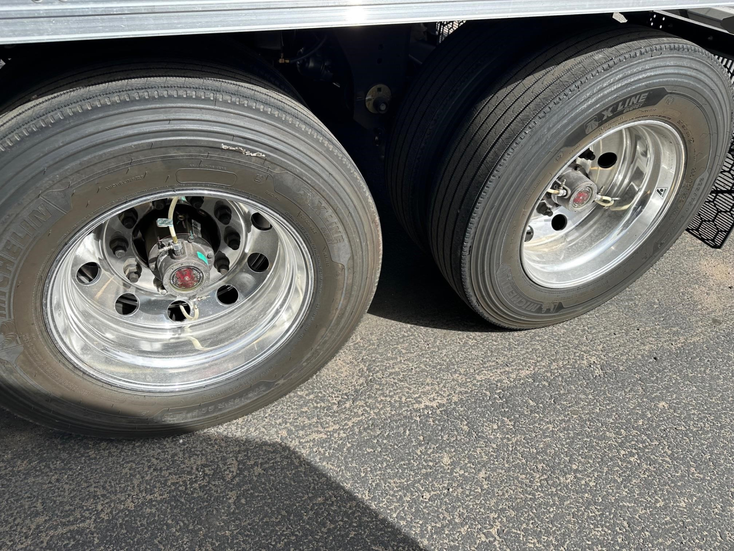 Trailer dual rear tires and chrome rims with metallic wheel hubs, undercarriage visible, side of reefer trailer in view.