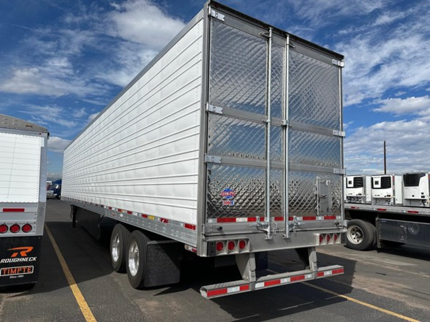 Trailer rear view showing double doors, diamond plate rear doors, and dual rear axles. Aluminum refrigerated trailer with textured doors and red-white reflective tape.