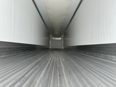 Trailer interior far end shows corrugated metal floor with sidewalls and ceiling, narrow aisle, reflective surfaces