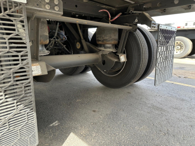 Trailer rear undercarriage showing wheels, suspension, and fuel/air lines for a 2026 Utility 3000R reefer trailer, with mud flaps and ribbed deck side.