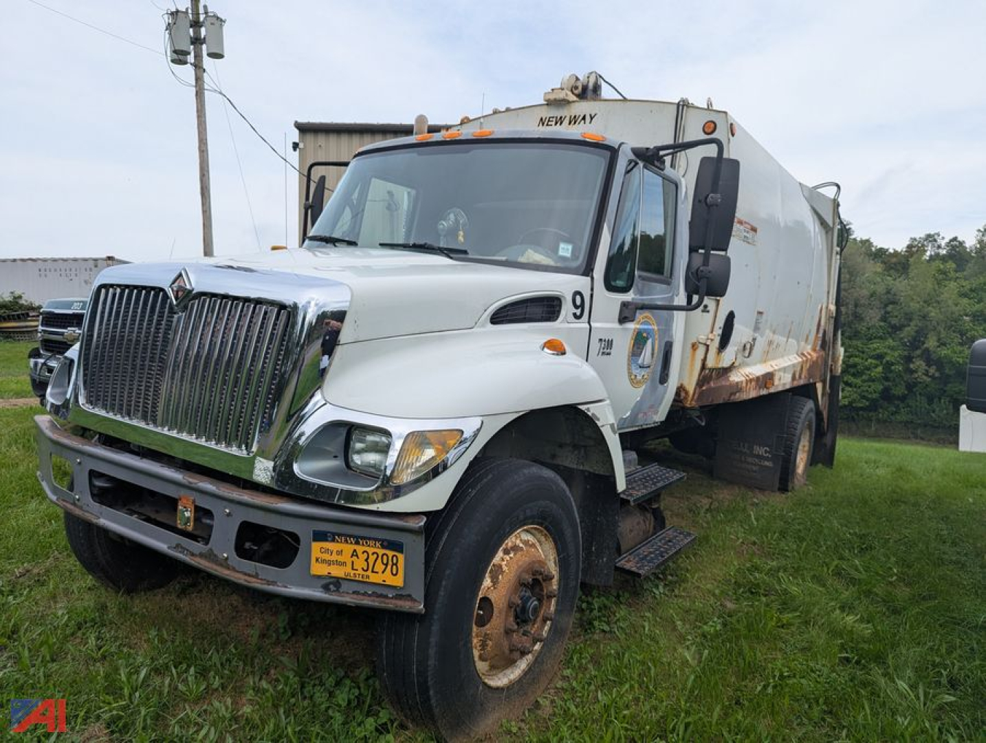 2005 International WorkStar 7300 20yd packer truck with front chrome grille, white cab, spoil truck bed, New York plates, on grassy lot.