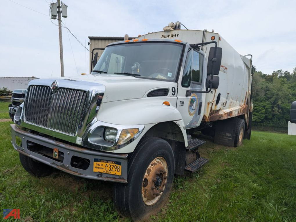 2005 International WorkStar 7300 20yd packer truck with front chrome grille, white cab, spoil truck bed, New York plates, on grassy lot.