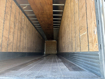Trailer interior showing wood-sided cargo area, vertical side panels, metal floor with ribbed texture, and open rear doorway.