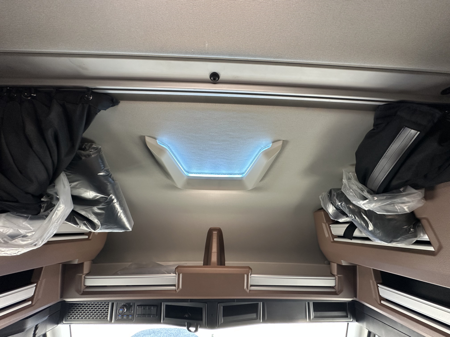 Interior cab viewing ceiling of a 2026 Mack PR64T64 sleeper showing overhead storage and skylight with plastic-wrapped components.