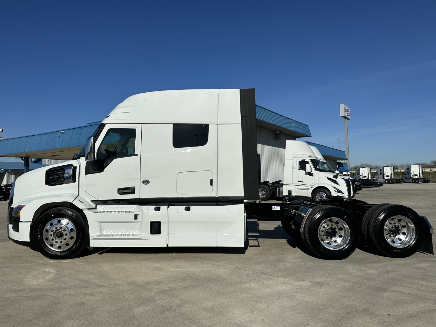 Side view of a white Mack PR64T64 tractor with a raised sleeper, showing dual rear axles and chrome wheels; no visible text legible on the image.