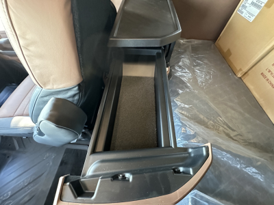 Truck interior center console open showing storage drawer with foam liner, beige seat edge and surrounding plastic trim.