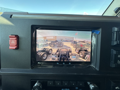 Dashboard view with screen showing a trailer and yard scene; hazard button on left and controls on right.