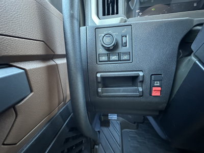 Dashboard controls and small central panel in a Mack PR64T64 truck cockpit with circular multi-function knob, several small toggle buttons, and empty storage pocket.