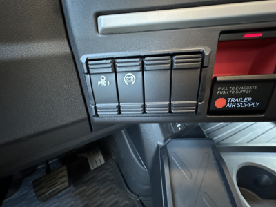 Dashboard area showing three switch buttons and a red-lit panel on Mack PR64T64 truck interior.