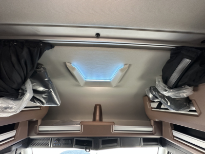 Interior cab viewing ceiling of a 2026 Mack PR64T64 sleeper showing overhead storage and skylight with plastic-wrapped components.