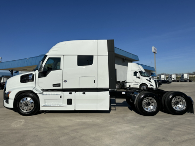 Side view of a white Mack PR64T64 tractor with a raised sleeper, showing dual rear axles and chrome wheels; no visible text legible on the image.