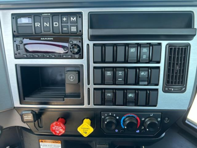 Mack AN64T instrument cluster and control panel showing gear selector R N D with M toggle, radio unit, multiple switch blocks, climate controls, and colored warning knobs.