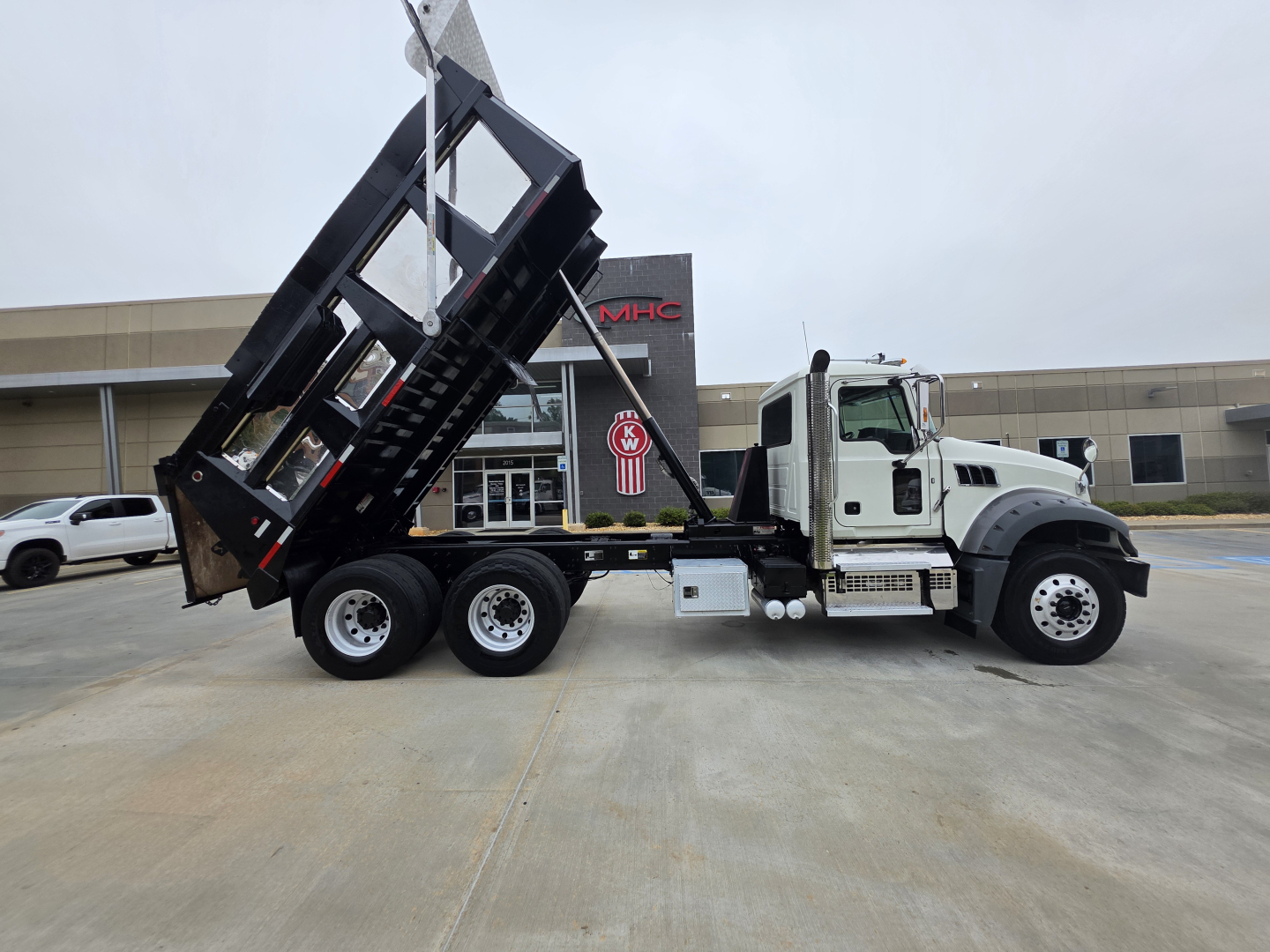 Dump truck side view showing raised bed on a 2022 Mack Granite with white cab and black dump body.