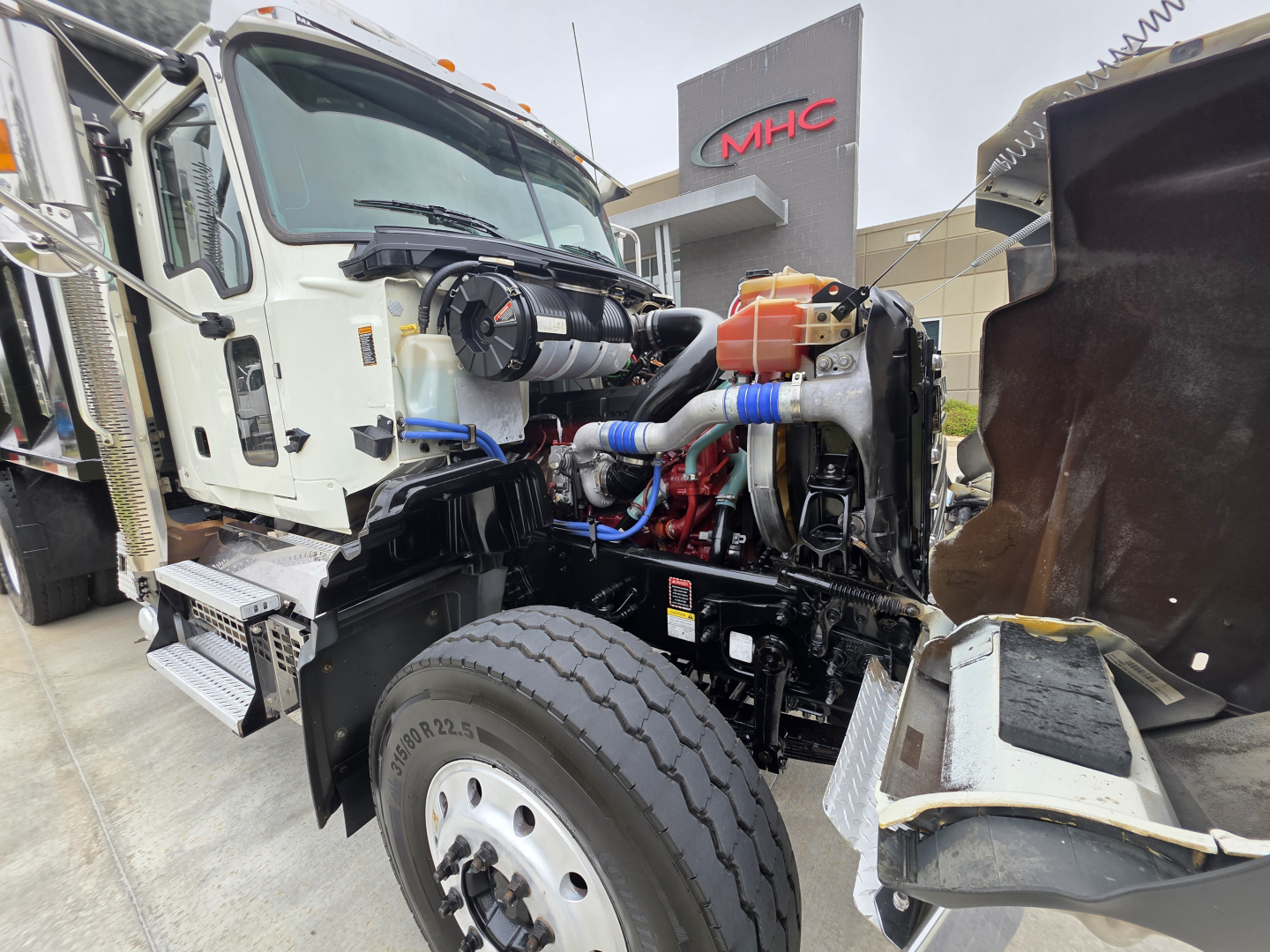 Front-left engine bay of a 2022 Mack Granite dump truck showing engine components, hoses, and hydraulic reservoir.
