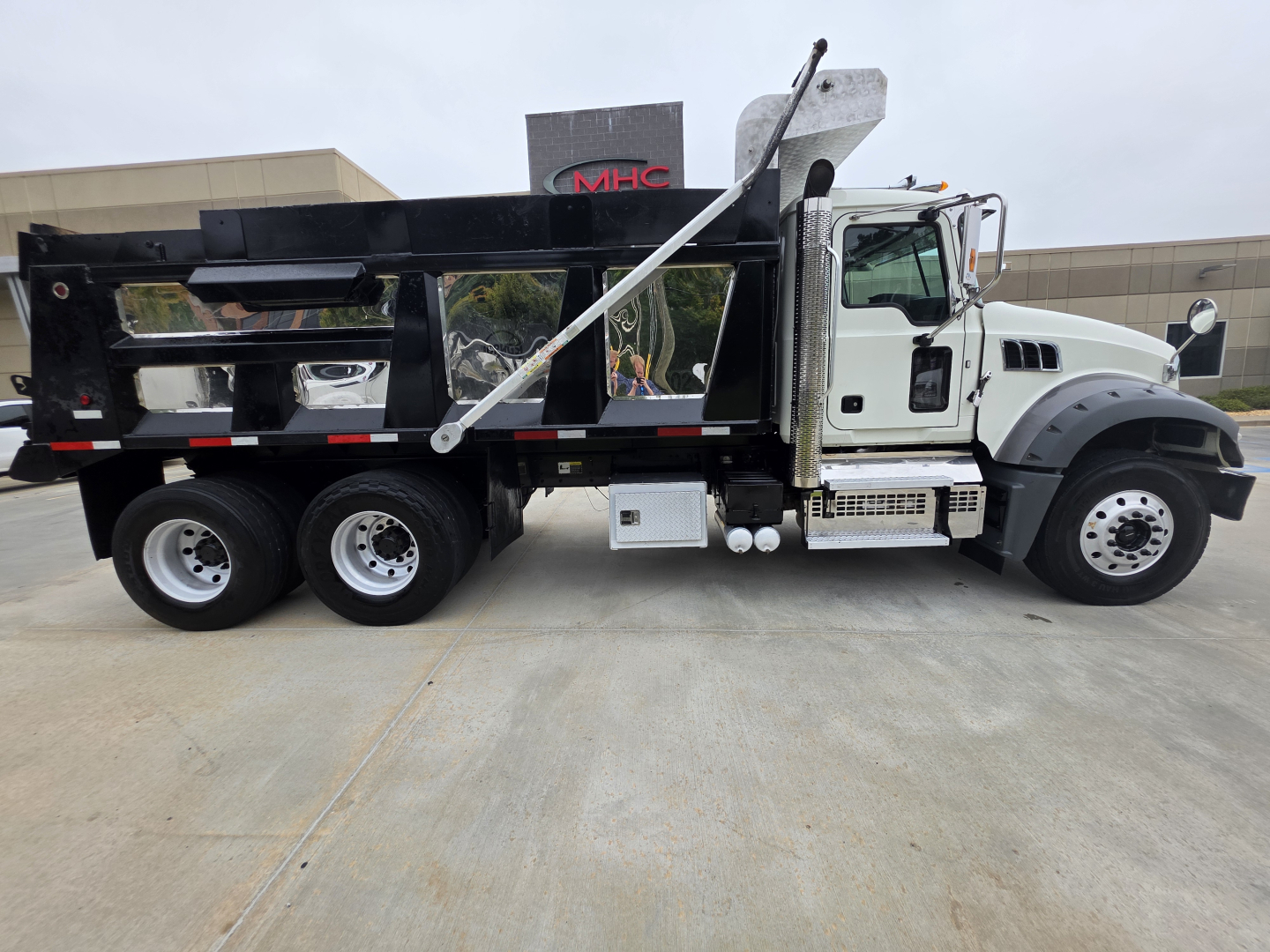 Dump truck side view showing hydraulic hopper and Mack Granite cab with white and black color scheme.