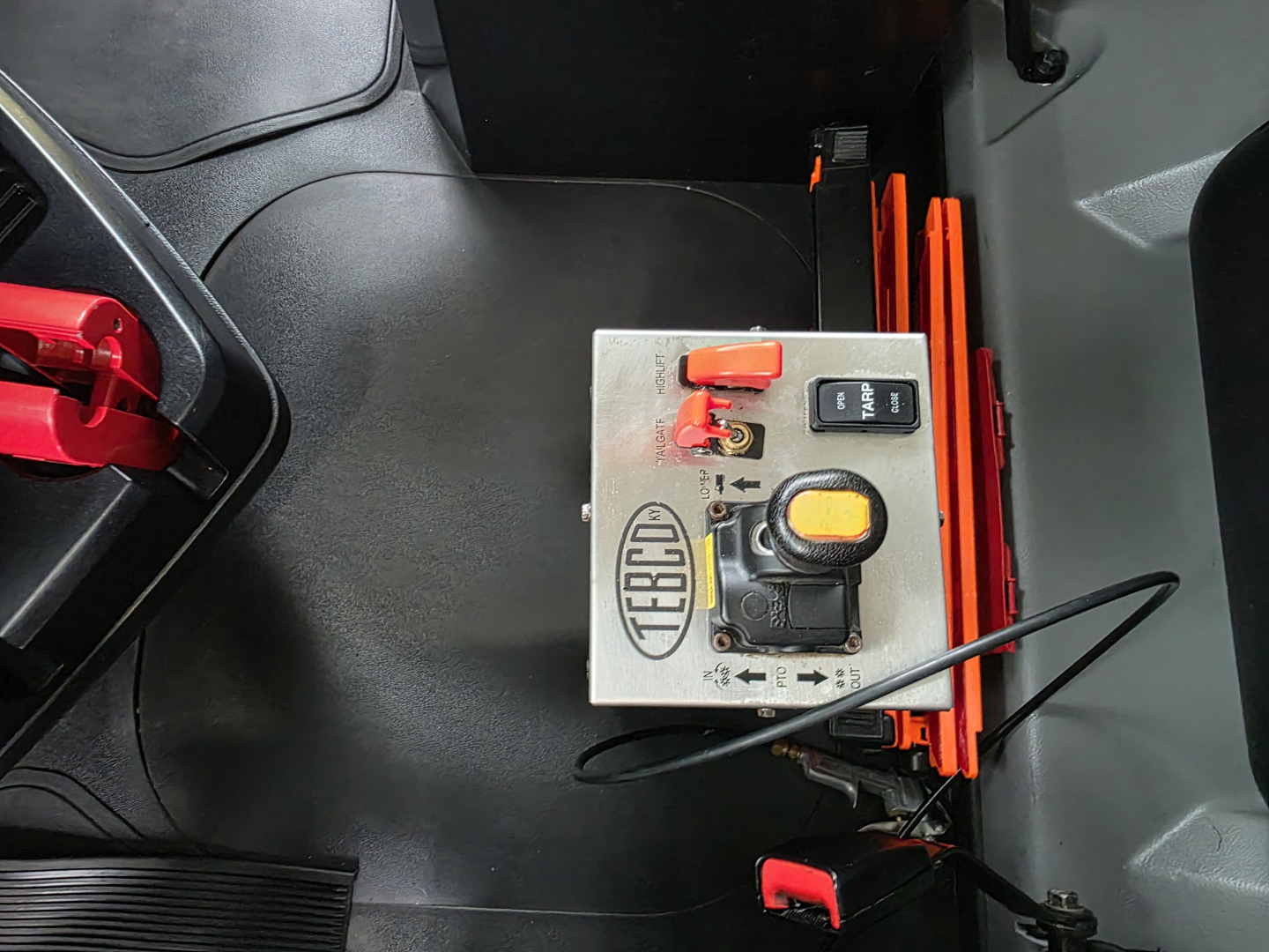 KOMATSU? Mack Granite truck interior with control module and orange levers; close-up of metal control box labeled with a circular logo and a yellow button.