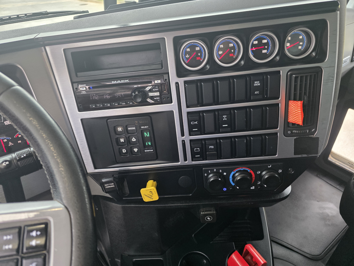 Dashboard view of a 2022 Mack Granite dump truck cab showing gauge cluster, aftermarket radio, climate controls, ignition key, and compact auxiliary switches.