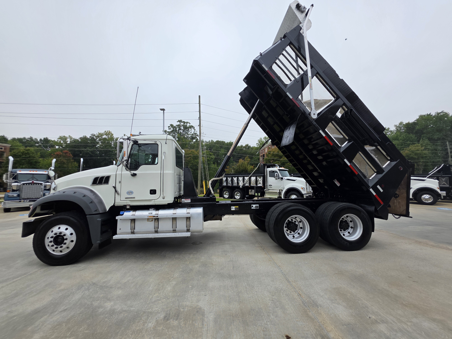 Dump truck side view showing a white Mack Granite truck with a raised black dump bed, dual rear axles, and a long wheelbase.