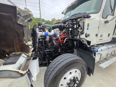 Truck engine bay of a 2022 Mack GRANITE dump truck showing exposed engine components, hoses, and intake with front wheel visible.