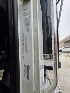 Truck door frame with small white labels and barcodes, interior latch area of a Mack Granite dump truck showing VIN sticker and warning labels.