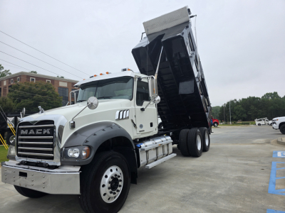 Mack Granite dump truck with its bed raised in a lot, white cab, large chrome grille, dual rear axles, and raised black dump bed.
