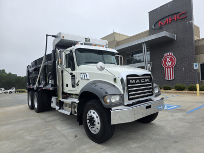 Mack Granite dump truck in service bay showing front grille with Mack emblem, chrome bumper, and dump body; showroom in background.