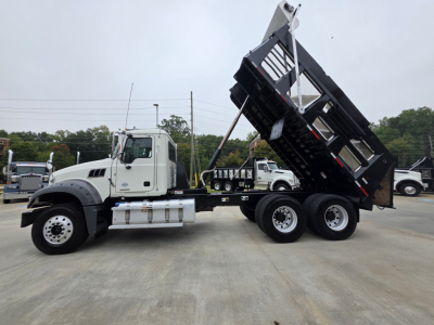 Dump truck side view showing a white Mack Granite truck with a raised black dump bed, dual rear axles, and a long wheelbase.
