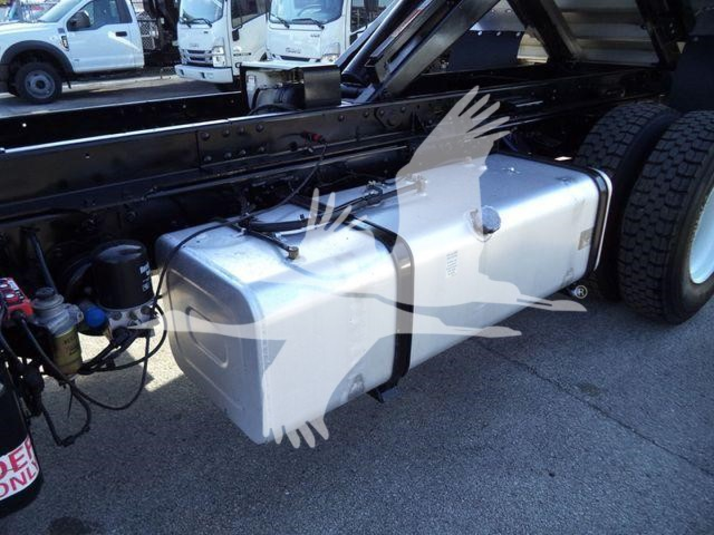 Isuzu FTR truck chassis showing a silver rectangular underbody fuel tank with mounting straps and adjacent engine components.