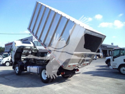 Isuzu FTR dump truck with bed raised in a yard; cab and chassis visible with other trucks in background.