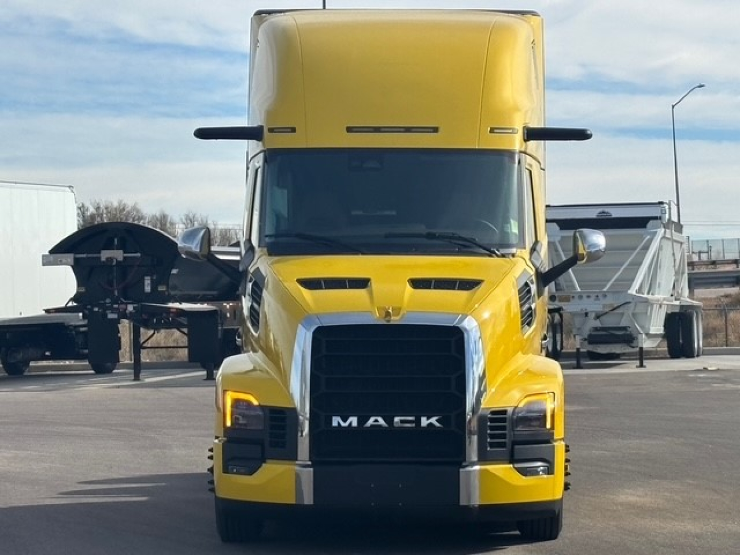 Front view of a yellow Mack PR64T76H truck with black grille, showing large front bumper and Mack logo.