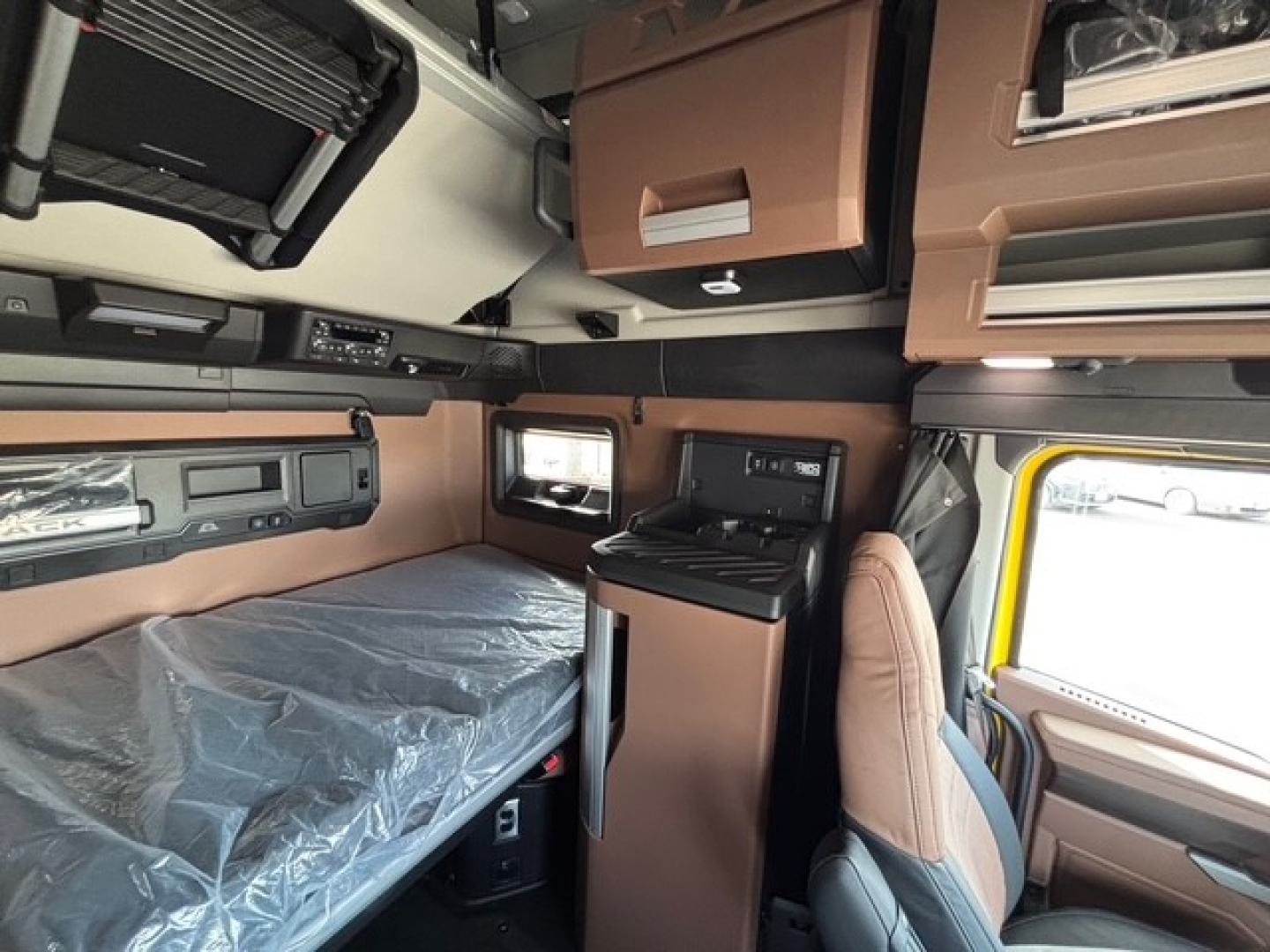 Interior of a new Mack PR64T76H sleeper cab showing bunk bed area, overhead storage, and cabin controls.