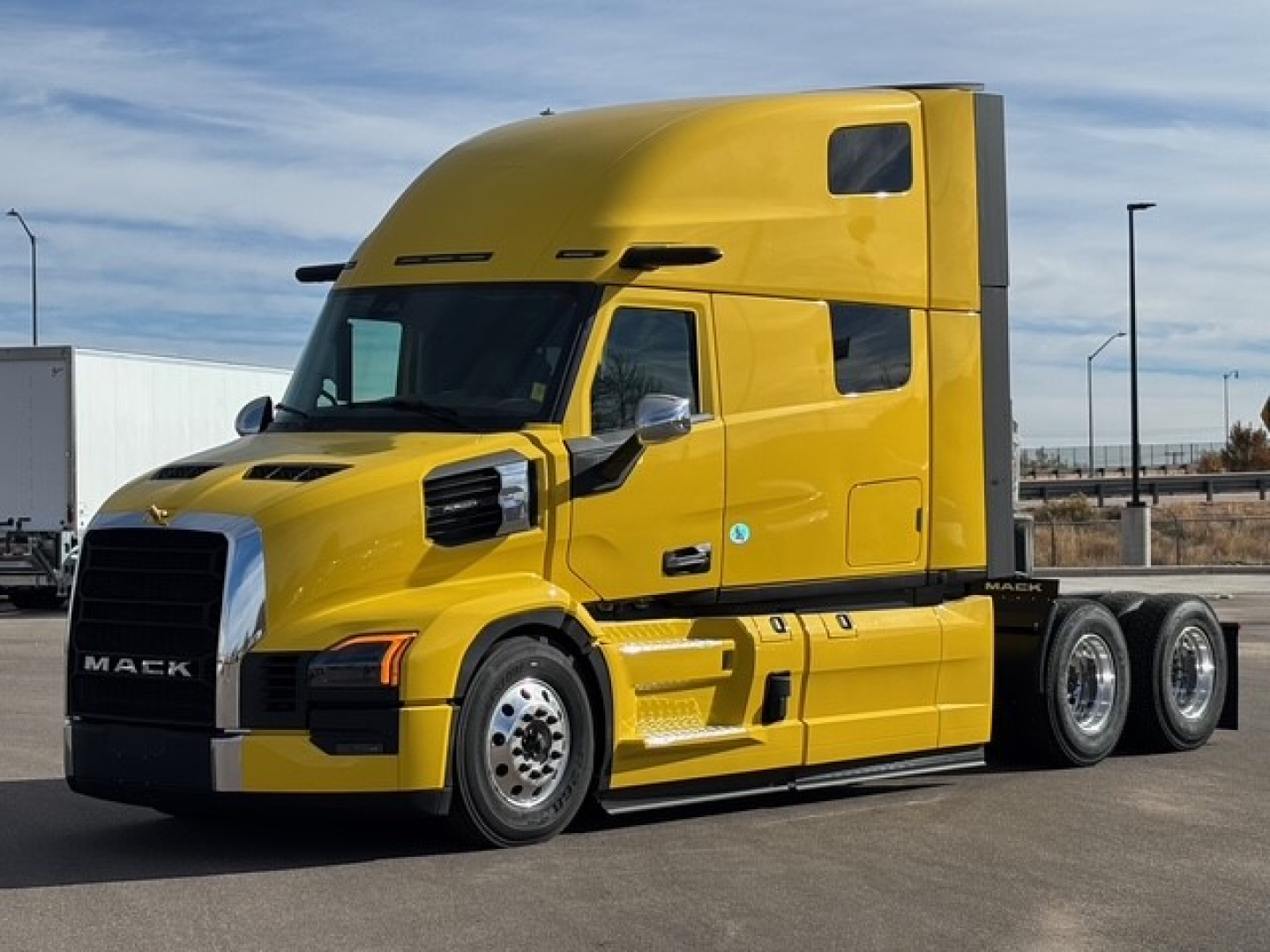 Yellow Mack PR64T76H tractor-trailer cab in side view showing front grille, large hood, sleeper cabin, and three rear axles with chrome wheels.