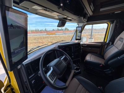 Cab interior of a 2026 Mack PR64T76H conventional sleeper showing steering wheel, dashboard, large mounted screen, and beige seats.