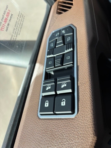 Truck interior panel with window/lock switches and mirror controls; brown textured trim; vertical arrangement of black buttons with white icons.