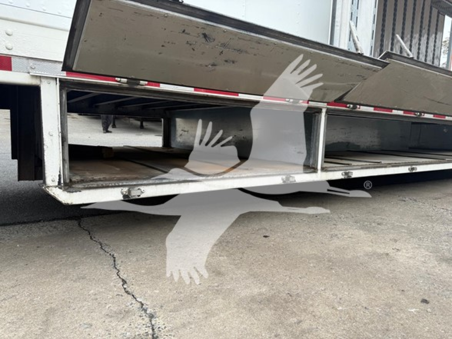 Trailer underside and wheel bay of a moving van trailer showing frame rails, reflective tape, and open undercarriage with metal supports.