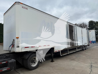 Moving van trailer side view showing white exterior with loading doors and tandem rear wheels.