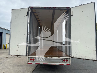 Trailer rear view showing open doors with empty moving van cargo space, wood floor, white exterior, VIN 1KKVE5322DL233955 and rear lights visible.