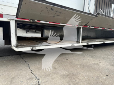 Trailer underside and wheel bay of a moving van trailer showing frame rails, reflective tape, and open undercarriage with metal supports.