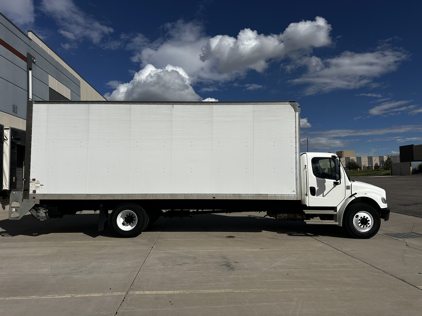 Truck side view of a 2022 Freightliner M2-106 box truck showing white cargo box and cab on a paved lot.