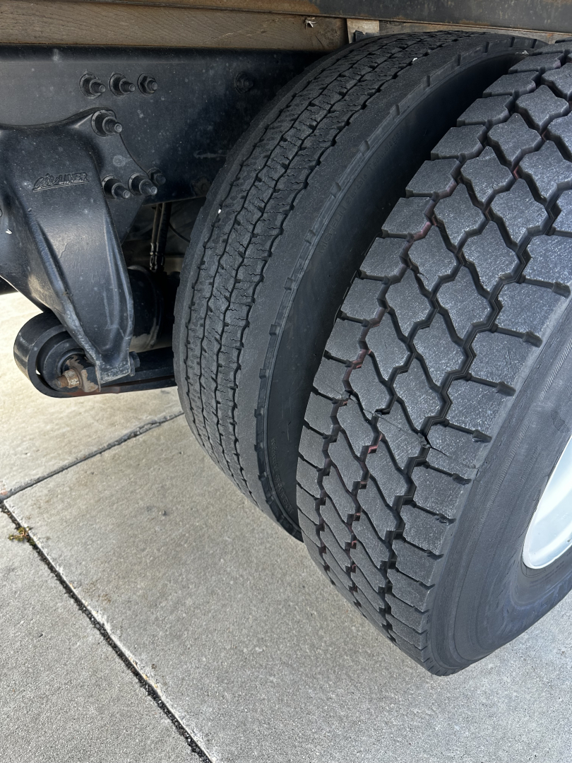 Truck wheel and suspension view showing dual rear tires and part of the frame from a Freightliner M2-106 undercarriage.