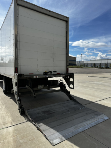 Freightliner M2-106 rear with hydraulic liftgate deployed; back of box truck visible with fold-down ramp and reflective lights.