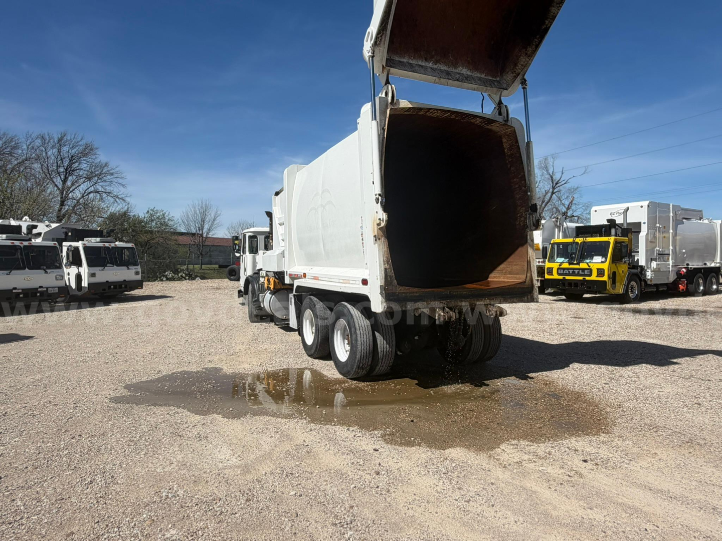 Autocar Xpeditor dump truck in a lot with rear bed raised, showing large open hopper and multiple wheels, others in background.