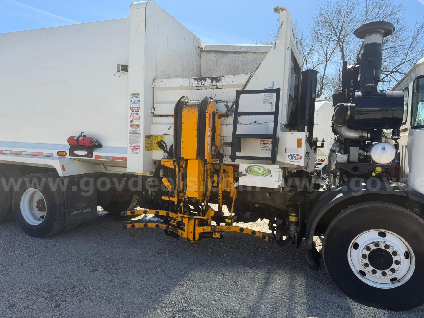 Autocar Xpeditor truck side view showing attached hydraulic overhead hoist and dump body with white cab and black engine area.