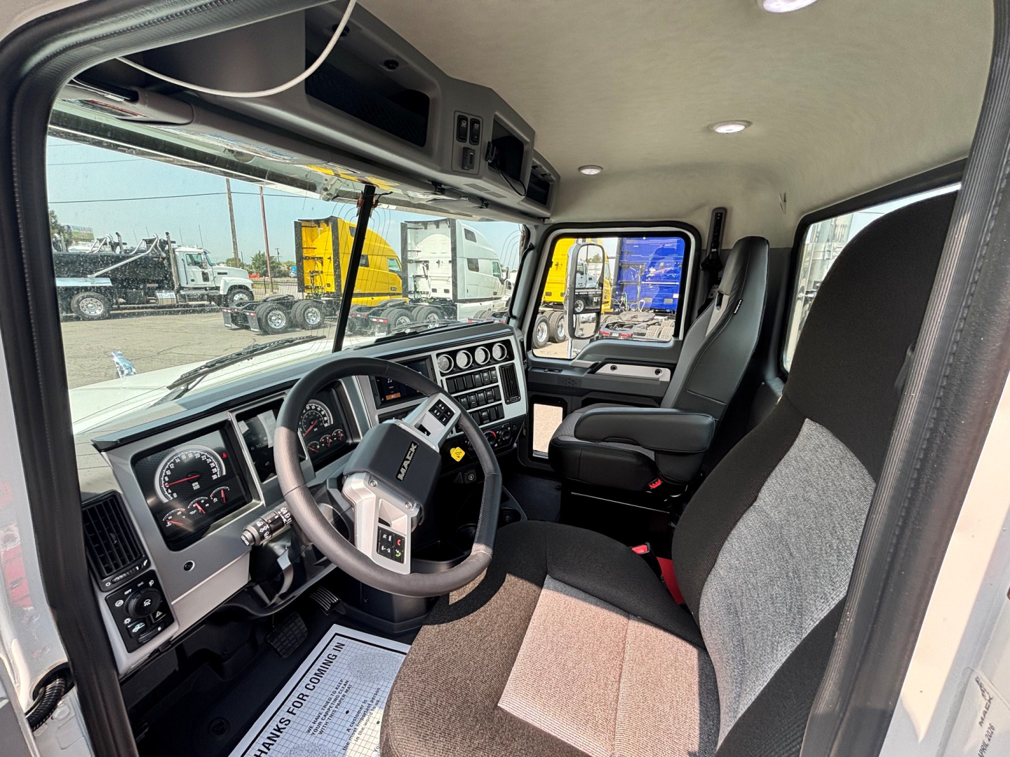 Interior of a new 2027 Mack PI64T daycab truck showing steering wheel, dashboard, and driver seat with gray and black trim.