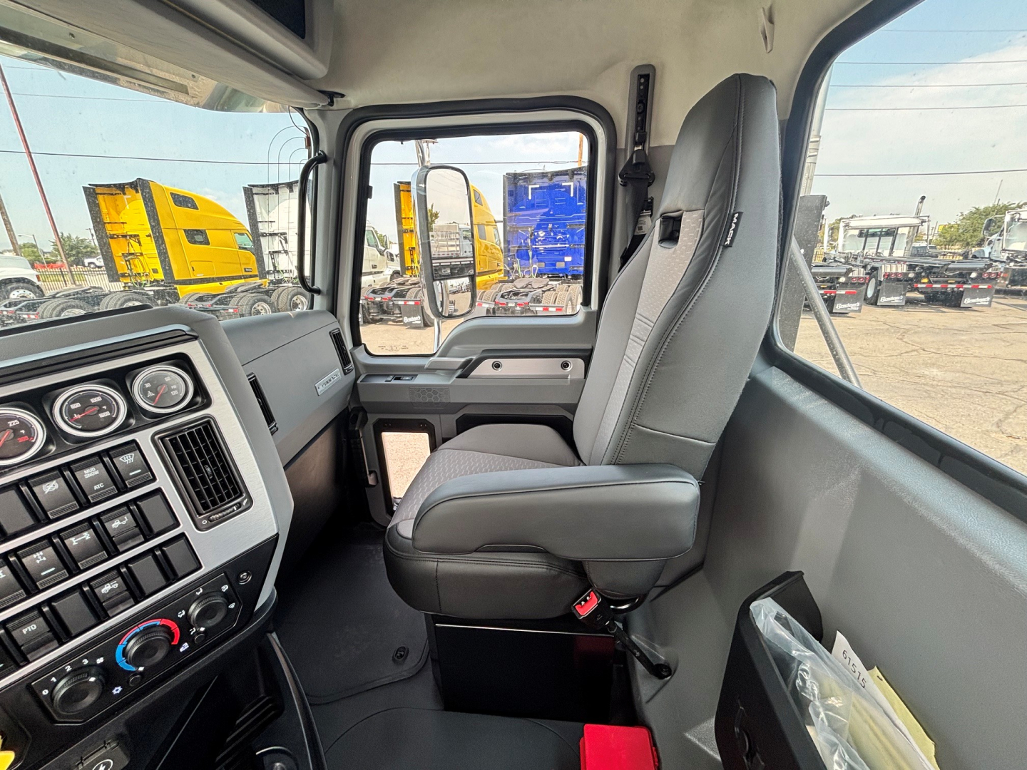 Cab view of a new Mack PI64T daycab showing driver's seat and dashboard with gauges and control panel.