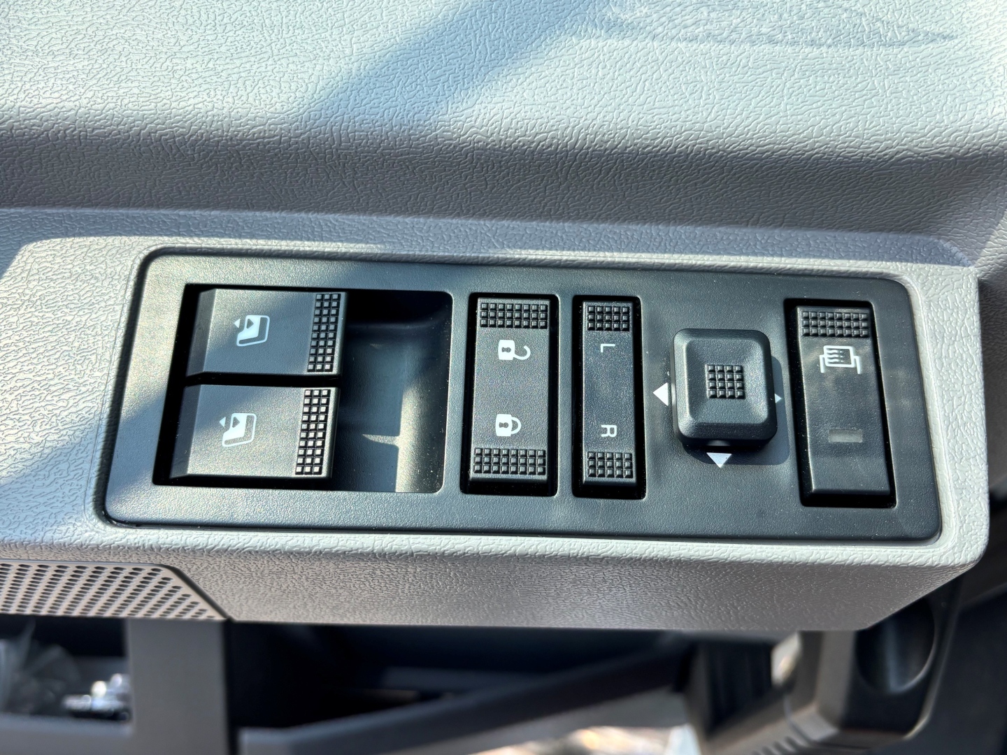 {Component} Driver door panel controls showing window and mirror switches, with surrounding textured dashboard on a Mack PI64T cab interior.