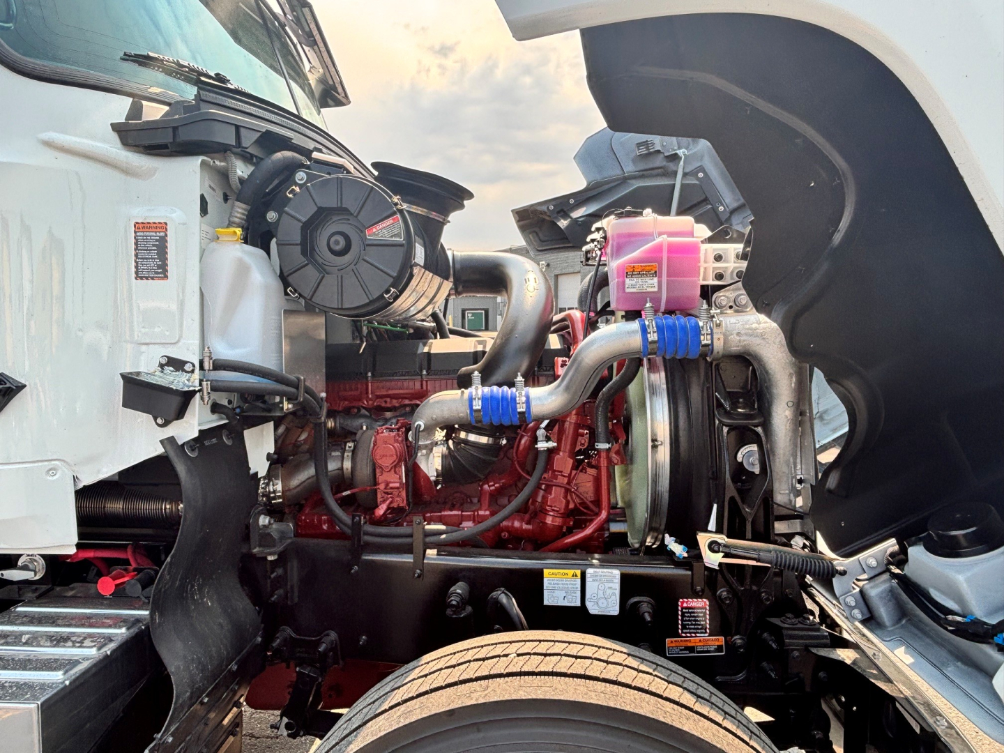 Mack PI64T engine bay showing turbocharger and intake piping with pink coolant reservoir and blue silicone hoses.