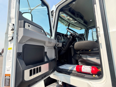 Mack PI64T truck cabin interior view with open door showing steering wheel, dashboard, and a red fire extinguisher on the floor.