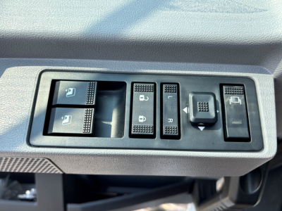 {Component} Driver door panel controls showing window and mirror switches, with surrounding textured dashboard on a Mack PI64T cab interior.