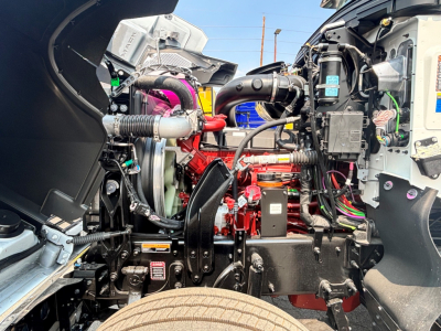 Mack PI64T engine bay showing high-performance engine components, hoses, and wiring harnesses; visible labels on coolant reservoir and nearby components.